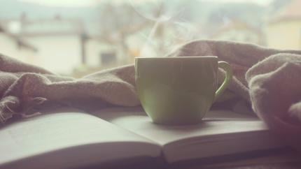 A steaming cup of coffee next to a book
