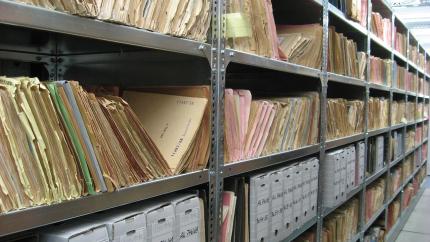 An archive shelf is shown filled with boxes ad documents
