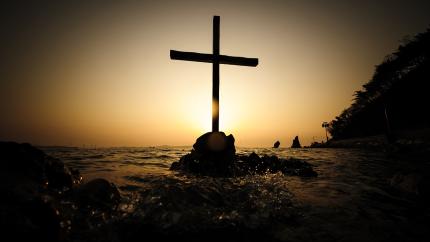 A cross stands with a bright background behind it.