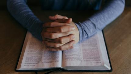 Hands folded in prayer over a biblical text