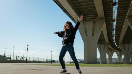 A woman does hip-hop dancing while standing under a large bridge