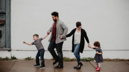 A family of four walks on a sidewalk holding hands