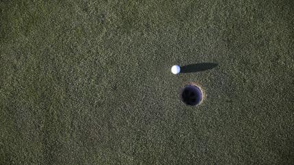 A golf ball slowly rolls towards a hole.
