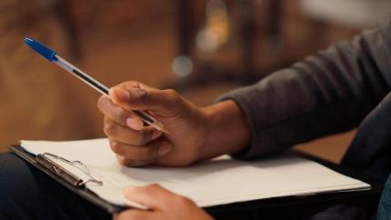 Photo of someone with a clipboard checklist, holding a pen in their right hand. 