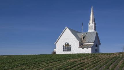 A church stands in the middle of a young green field. Courtesy of Pexels.