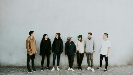 Image of a group of young adults standing against the background of a white wall. Courtesy of Pexels.