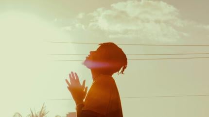 A man holds his head up towards the sky, his hands folded in prayer ahead of him. Courtesy of Unsplash.