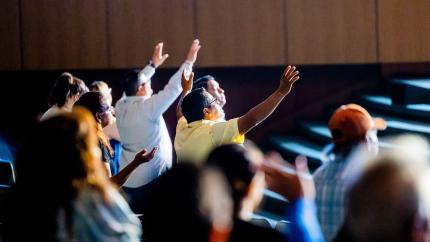 A community of people raise their hands together in worship. Courtesy of Pexels.