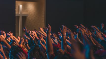 A group of people all raise their hands together in worship. Courtesy of Unsplash.