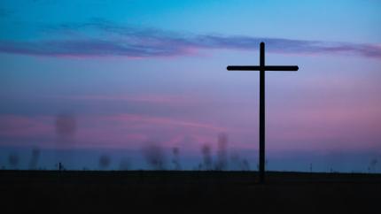 A cross stands against a sunset background. Courtesy of Unsplash.