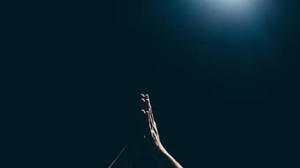 Image of hands at prayer held up against a black background. Courtesy of Unsplash.