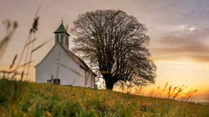 A church sits on a hill with the sun setting in the background. Courtesy of LN_Photoart on Pixaby.