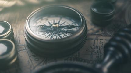 A directional compass sits on a map next to a magnifying glass.