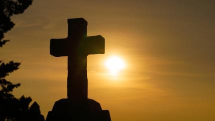 A cross stands silhouetted by a setting sun