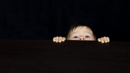 a baby peeks over the edge of a dark surface