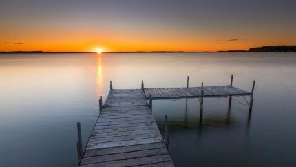 A pier reaches out into a lake. Courtesy of Unsplash.