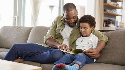 a father and son read a book together on a couch