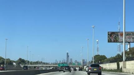 An individual in a car drives down a road looking towards the skyline of a large city.
