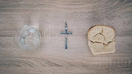 A photo of a glass, a cross, and a piece of bread on a table.