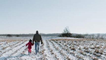 An old man walks through a snowy fielding holding the hand of a little boy