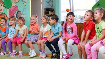 A group of kids stands together smilling while looking at a teacher. Courtesy of Pexels.