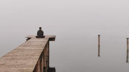Man sits on a pier looking over a gray lake