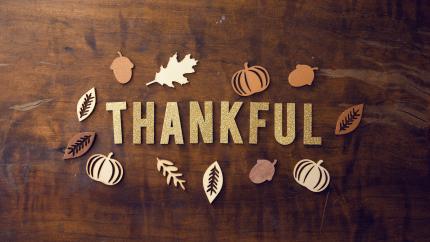 Words "thankful" are included against a wooden background with small decoration of pumpkins and fall leaves.