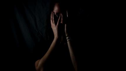 a silhouette of a woman in the dark, covering her face with her hands