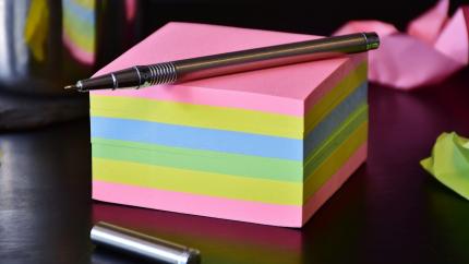 Stack of sticky notes with a pen sitting on top.