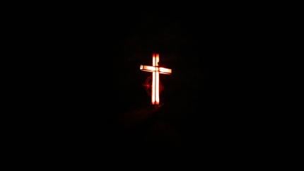 An image of a lit cross stands in the center of a dark background. Courtesy of Pixaby.