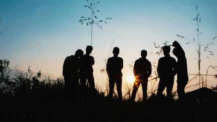 A group of young people hang out one evening. They are silhouetted with a blue sky background behind them.