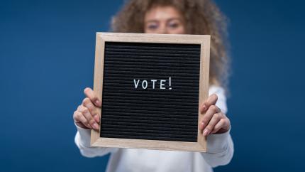 A woman holds out a sign that reads "vote"