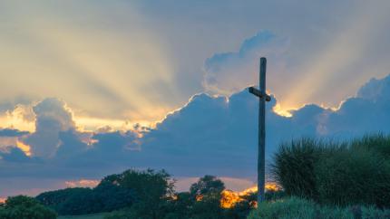 On a background of a setting sun, a cross stands on a hill