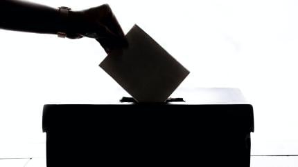 An individual puts a ballot into a ballot box