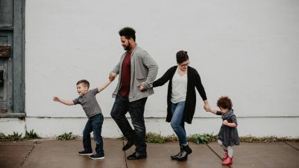 A family holds their kids' hands as they go on a walk in the rain.