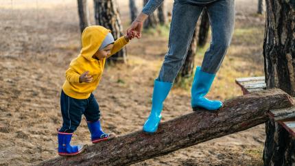 A child walks up a log, guided by their parent.