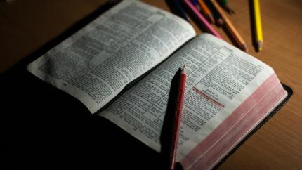 A bible stands on a wooden desk, surrounded by highlighters.