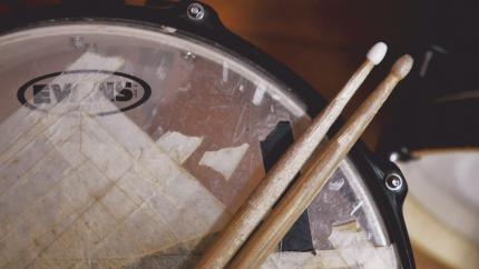 two drumsticks rest diagonally on a taped-up drum