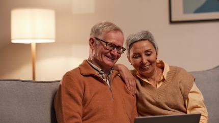 Two elderly people look at a computer while smiling