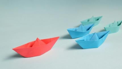 A single boat travels ahead of other boats, representing leadership