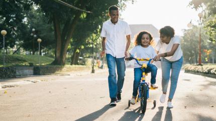 A girl is riding a bike, followed by her father and mother. Courtesy of Agung Pandit Wanga on Pexels.