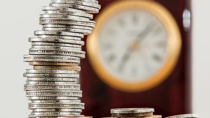 A stack of coins sits in front of an out-of-focus clock.