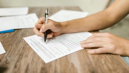 A handheld pen is filling in a form. Courtesy of Pexels.