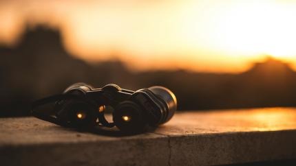 A pair of binoculars sits on a fence. Courtesy of Unsplash. 