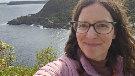 Kristen stands on a hill in Newfoundland overlooking the ocean.