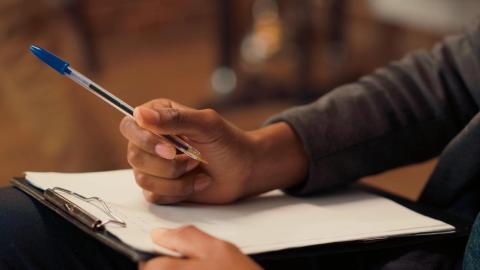 Photo of someone with a clipboard checklist, holding a pen in their right hand. 