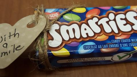 Box of Smarties candy, with handmade label attached that says, "With a Smile." 
