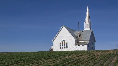A church stands in the middle of a young green field. Courtesy of Pexels.