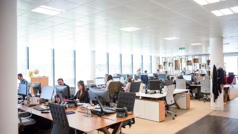 An image of a busy day at an office, with many people working at computers and chatting. Courtesy of Unsplash.