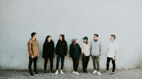 Image of a group of young adults standing against the background of a white wall. Courtesy of Pexels.